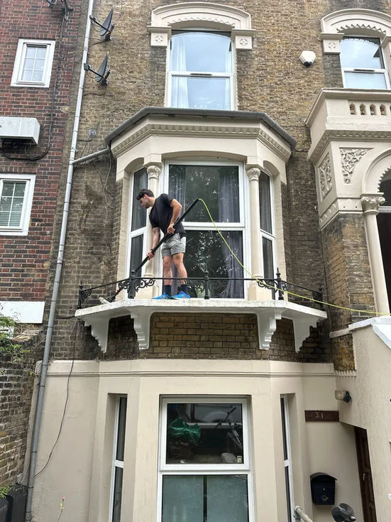 Cleaning a bay window from the balcony of a Victorian terrace in north London