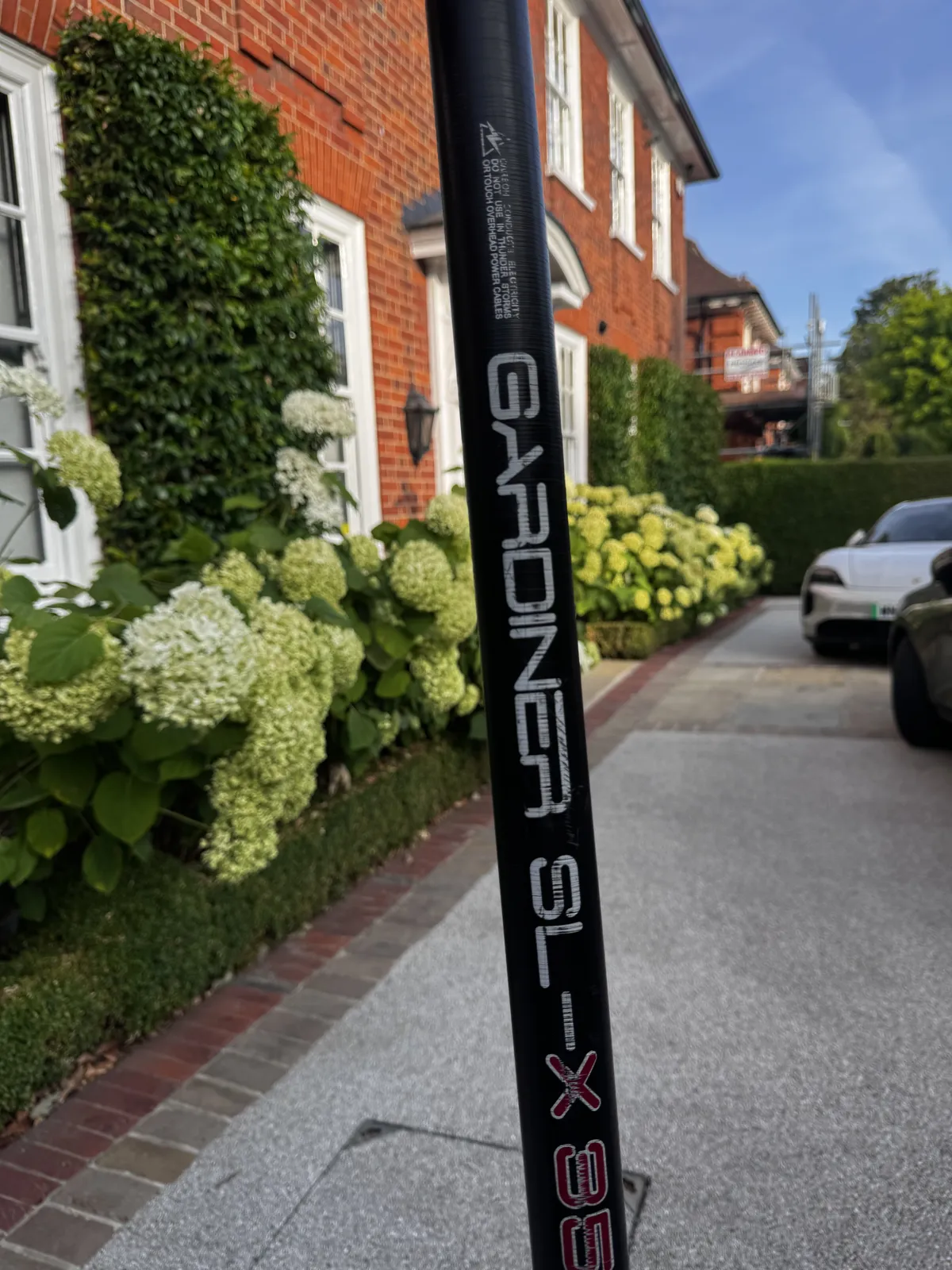Water-fed pole set up against a red brick house with hydrangeas in the front garden