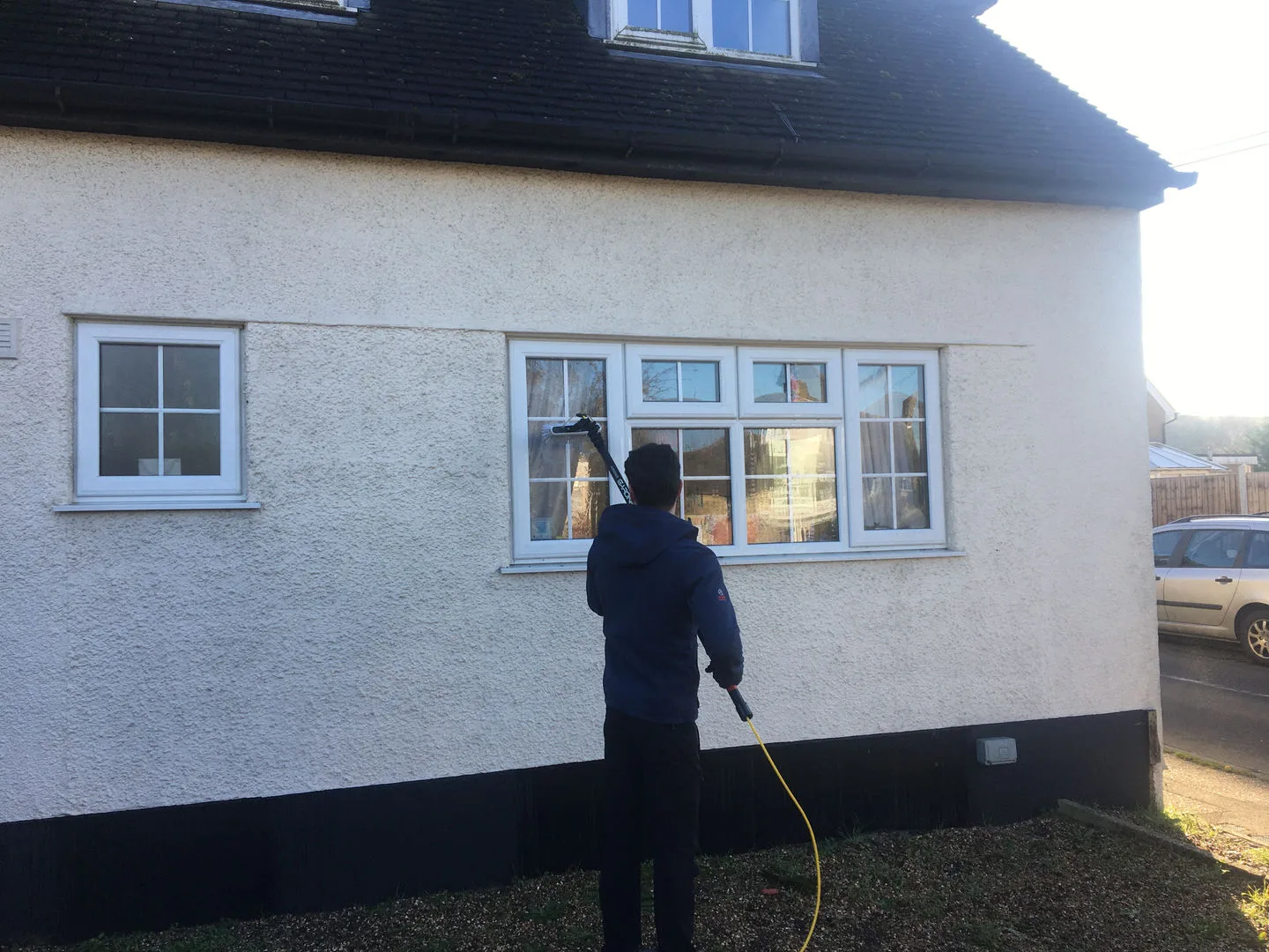 Cleaning the windows of a white rendered house with a water-fed pole