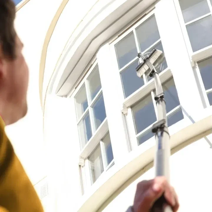 Cleaner using a water-fed pole on the windows of a curved white period building